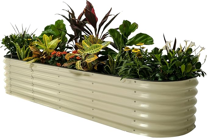 A long, rectangular, beige metal planter box filled with an assortment of green, yellow, and red-leafed plants, including flowering plants with white and yellow blooms.