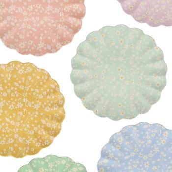 Scalloped-edge plates in pastel pink, yellow, green, and blue, each with a white floral pattern, are artfully arranged against a white background.