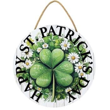 Round wooden sign with a large green shamrock surrounded by white daisies in the center. The words "Happy St. Patrick's Day" curve around the edge. The sign has a rope for hanging.