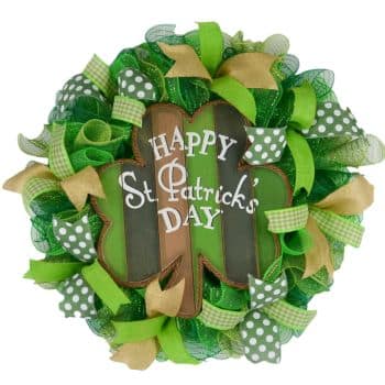 A circular St. Patrick's Day wreath featuring a large shamrock shape with green and tan stripes. It has "Happy St. Patrick's Day" written on it and is adorned with green ribbons, polka dots, and plaid patterns.