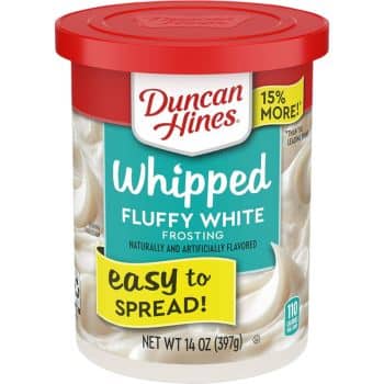 Container of Duncan Hines Whipped Fluffy White Frosting with a red lid. Perfect for your favorite spring cookies, the label highlights "15% more," "easy to spread," and "naturally and artificially flavored." Net weight is 14 oz (397g).