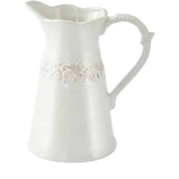 A white ceramic pitcher with an ornate handle and embossed floral designs around the middle, featuring a wide spout and a slightly curvy top edge.