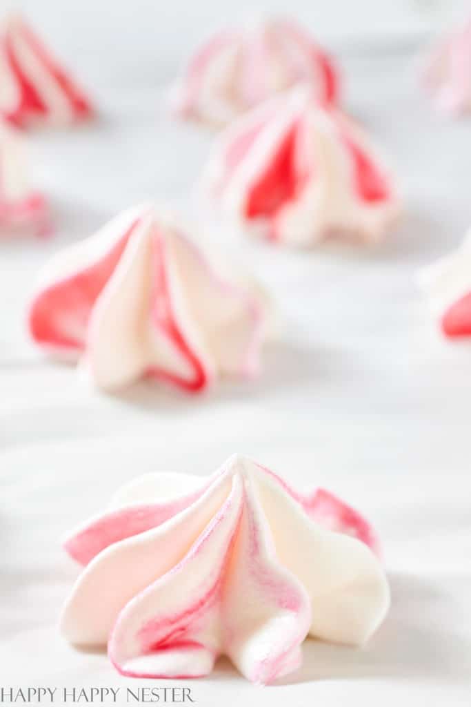 Pink and white meringue cookies, your favorite spring cookies, are artfully arranged on a white surface. These delicate treats boast a swirled pattern and a soft, airy appearance, highlighting their light, fluffy texture.