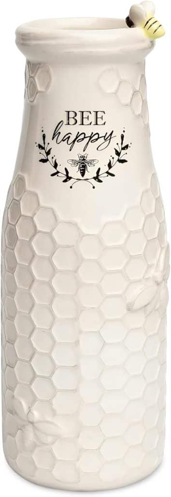 A white ceramic vase with a honeycomb pattern, embossed bees, and the phrase "BEE happy" is perfect for spring kitchen decor. Featuring leafy accents and a small ceramic bee perched on the rim, it brings cheerful charm to your space.