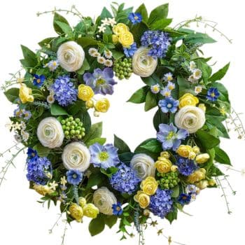 A circular floral wreath made of white, yellow, and blue flowers, accented with green leaves and small green berries—perfect for adding a fresh touch of spring kitchen decor against a white background.