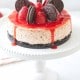 Decadent strawberry cheesecake topped with whole chocolate sandwich cookies and fresh strawberries, drizzled with a vibrant red sauce, sits on a white cake stand against a soft background.