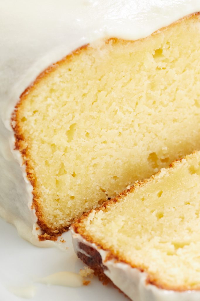 Close-up of one of the best spring cakes—a sliced lemon pound cake with thick, glossy white icing. The cake appears moist with a light, golden-brown crust. Its dense and smooth texture reveals a rich yellow color inside.