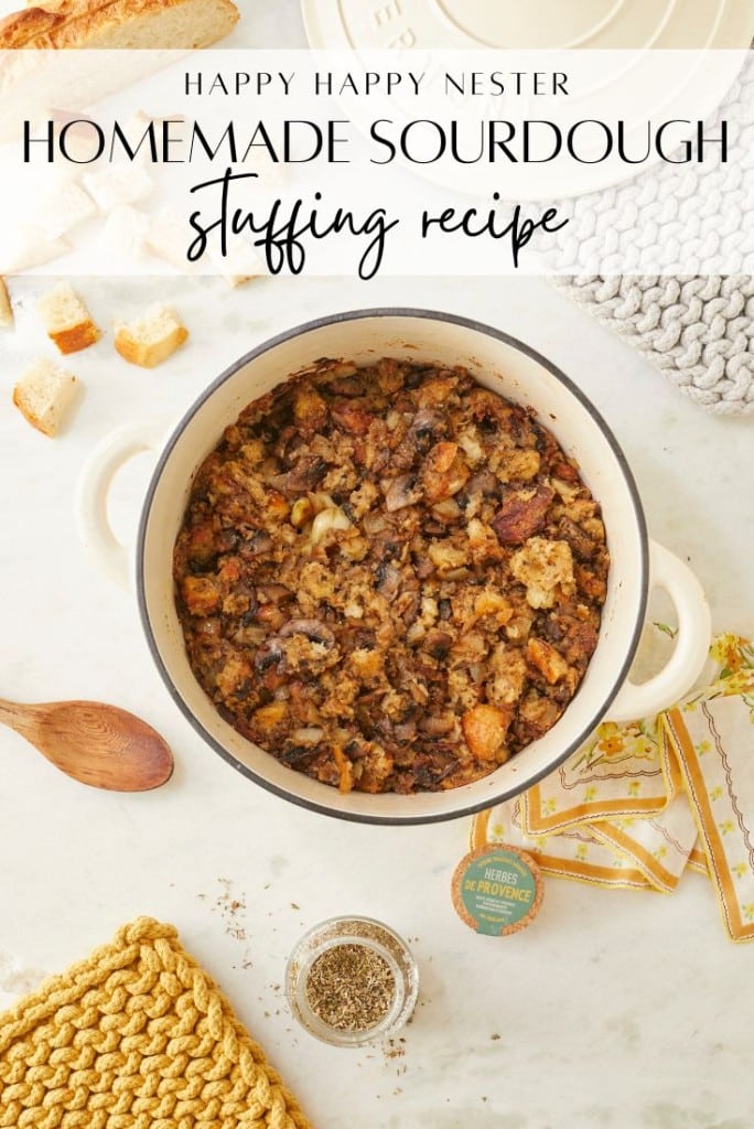 Top view of a pot brimming with a delightful homemade sourdough stuffing recipe on a white marble surface. Surrounding items include a wooden spoon, chunks of bread, herbs, and decorative cloth. Text on the image reads "Homemade Sourdough Stuffing Recipe.