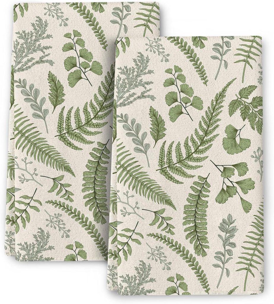 Two beige kitchen towels with a repeating pattern of green fern and botanical leaf illustrations, arranged diagonally. Perfect as spring kitchen decor, the design brings a fresh, natural, outdoorsy feel to your space.