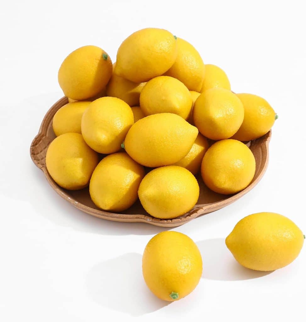 A brown ceramic plate filled with bright yellow lemons sits on a white surface, with three more lemons scattered nearby—an inviting touch of spring kitchen decor.