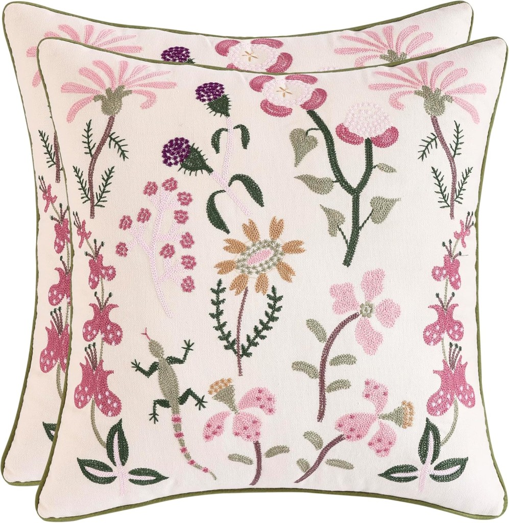 Two square decorative pillows with colorful floral embroidery featuring pink, purple, and green flowers and leaves on a cream background. Each pillow has a green border.
