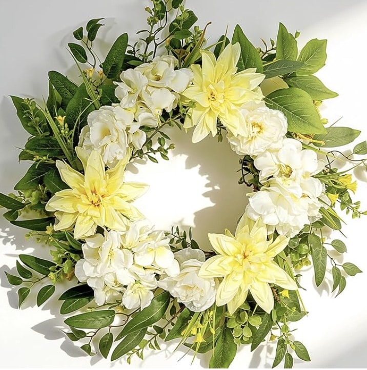 A circular floral wreath with yellow and white flowers, including dahlias and roses, surrounded by lush green leaves, displayed on a white background—perfect for those seeking colorful summer wreaths.