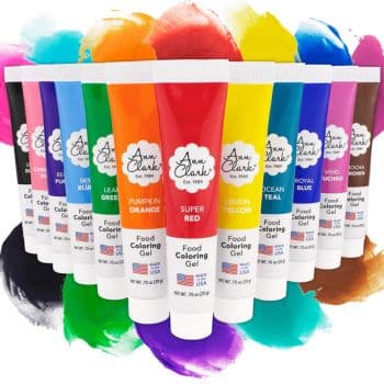 Twelve tubes of Ann Clark food coloring gel in vibrant hues are arranged in a semi-circle, with colorful splashes behind them—perfect for decorating your favorite summer cookies and showcasing the full range of available colors.