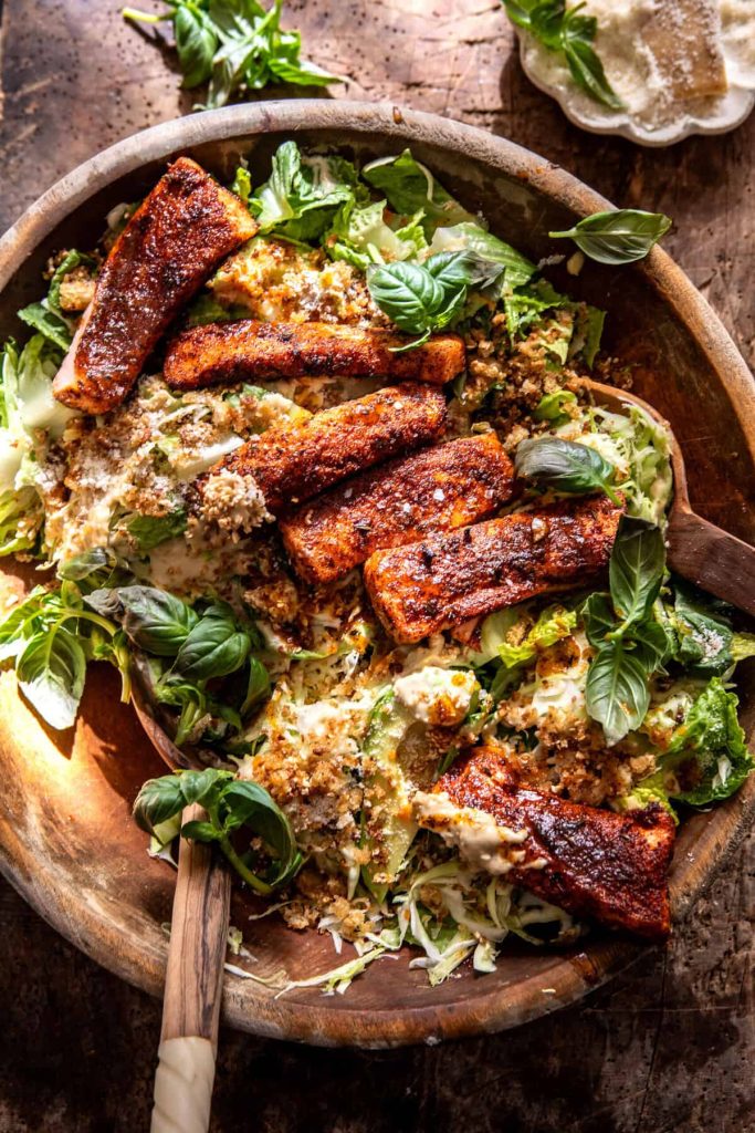 A wooden bowl filled with leafy green salad, topped with seasoned and browned fish fillets, creamy dressing, fresh basil leaves, and a wooden serving spoon—one of my favorite easy dinner ideas.