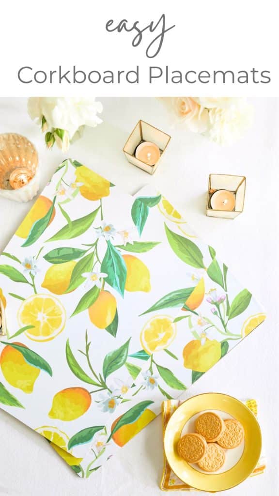 Flatlay of some lemon decorated placemats on a white table cloth. There are candles votives and a dish of cookies on the table as well. The placemats are homemade an part of an easy corkboard placemats diy project. 