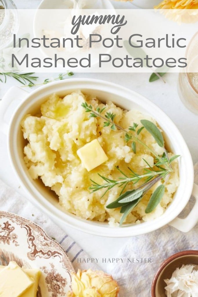 A white oval dish filled with mashed potatoes, topped with butter and fresh herbs, sits on a light table. The text reads "Yummy Instant Pot Garlic Mashed Potatoes Recipe." Various plates and ingredients surround the dish.