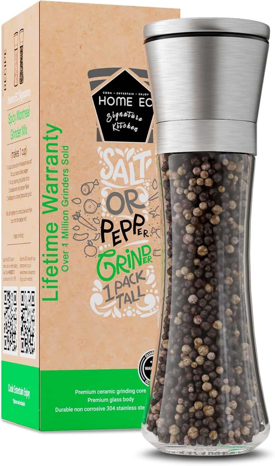 A glass pepper grinder with a stainless steel top sits by its box, labeled with phrases like "Lifetime Warranty" and "Salt or Pepper Grinder." Filled with peppercorns, it's perfect for seasoning when learning how to make a tender juicy steak.