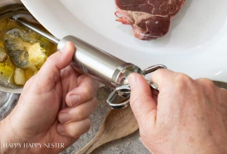A person fills a stainless steel meat injector with marinade from a bowl, preparing to inject it into a raw steak on a white plate—a key step in how to make a tender juicy steak. A wooden spoon and the edge of a towel are nearby.