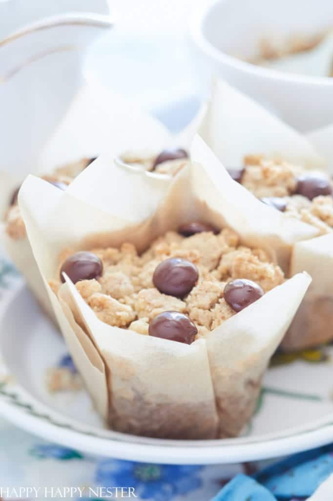 Close-up of a muffin with a crumbly streusel topping and several chocolate-covered coffee beans—one of my favorite chocolate recipes—wrapped in parchment paper and placed on a white plate with a floral design.