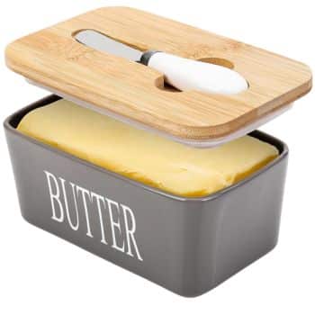A gray butter dish labeled "BUTTER" holds a slab of butter, perfect for pairing with my favorite side dishes. The wooden lid, partially open, has a slot holding a small butter knife with a white handle.