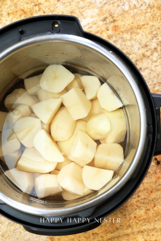 Peeled and chopped potatoes soaked in water inside an Instant Pot on a granite countertop, ready to be made into instant pot garlic mashed potatoes.