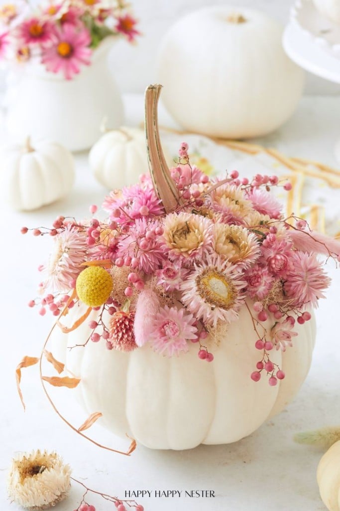 A white pumpkin is decorated with a colorful arrangement of pink and yellow dried flowers, surrounded by more white pumpkins and floral accents—one of my favorite flower crafts for brightening any light, airy space.
