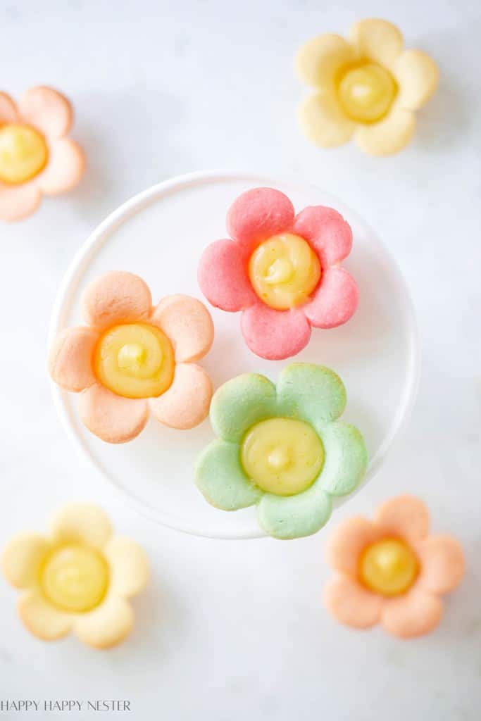 Colorful flower-shaped cookies with creamy yellow centers are arranged on a white plate and surface, inspired by my favorite flower. The pastel pink, yellow, green, and orange treats create a bright, cheerful setting.