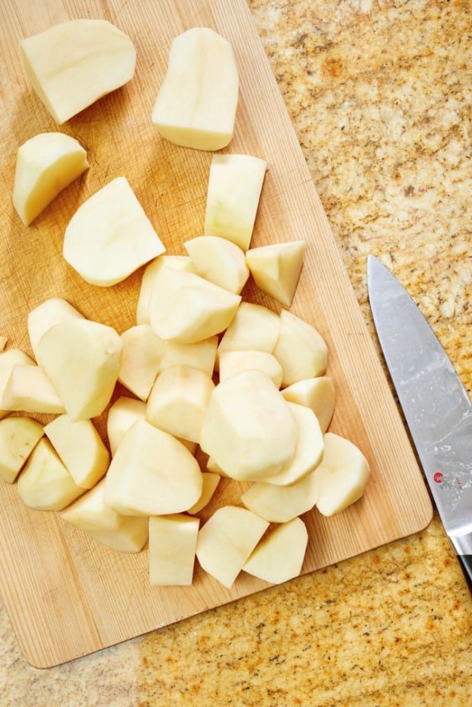 Peeled and chopped potatoes on a wooden cutting board, ready to be transformed into creamy Instant Pot garlic mashed potatoes, with a chef’s knife resting nearby on a granite countertop.