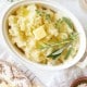 Oval white dish filled with creamy Instant Pot garlic mashed potatoes, topped with a pat of butter and garnished with fresh herbs. Surrounding the dish are plates, butter, a napkin, and a small bowl on a light background.