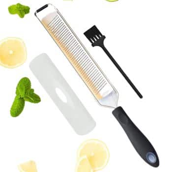 A citrus zester with a black handle, a protective cover, and a small cleaning brush is shown alongside scattered lemon slices—perfect for adding zest to my favorite side dishes—and mint leaves on a white background.