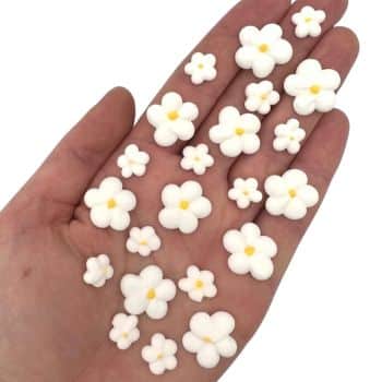A hand holding several small, white, five-petal flower decorations with yellow centers, arranged in rows of different sizes—my favorite flower inspiration captured in every delicate detail.