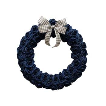 A circular wreath made of dark blue fabric roses, adorned at the top with a black and white checkered bow. The background is plain white.