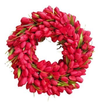 A circular wreath made of numerous bright red tulips with green leaves, arranged closely together in a full, vibrant display against a white background.
