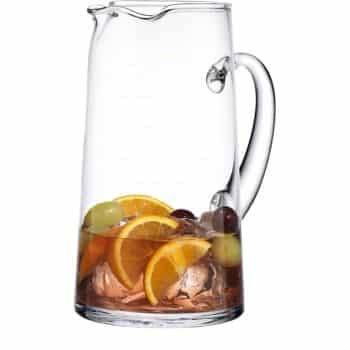 A clear glass pitcher with a handle, partially filled with ice cubes, orange slices, and green and red grapes—perfect for serving my favorite summer drinks. The pitcher is empty except for the fruit and ice.