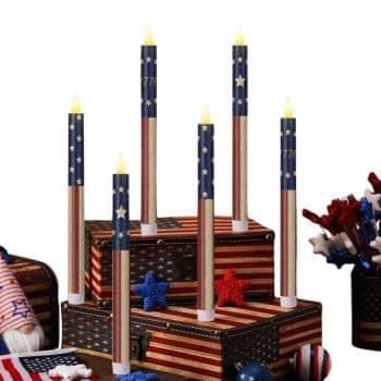 Six LED candles with American flag designs are displayed on vintage suitcases decorated with stars and stripes. Patriotic decorations, such as pinwheels and star shapes, are arranged around the scene.