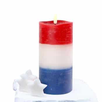A lit pillar candle with three horizontal stripes: red on top, white in the middle, and blue at the bottom. Two white star-shaped candles sit beside it on a white surface.