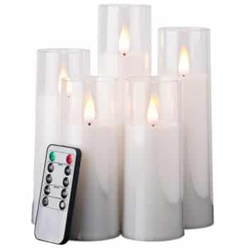 Five white flameless LED candles in tall, clear glass holders are grouped together. In front, there is a remote control with buttons, used to operate the candles.