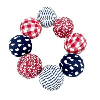 Eight fabric balls arranged in a circle, featuring various patterns including red and white checkered, blue and white striped, red with white floral, and blue with white polka dots.