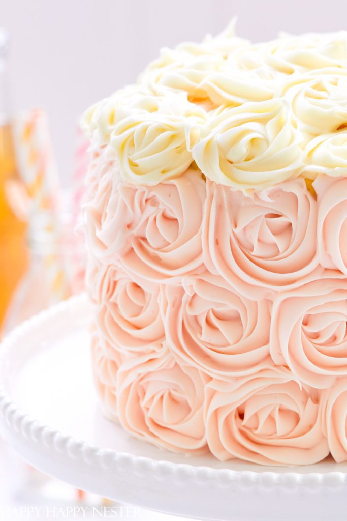 A cake decorated with pink and white buttercream roses sits on a white cake stand. The rosette pattern creates an elegant, floral look—truly one of my favorite floral desserts.