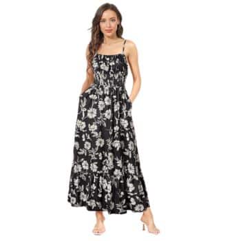 A woman wearing a black sleeveless maxi dress with white floral patterns and ruffled hem, standing with her hands in her pockets and wearing clear-strap heels.