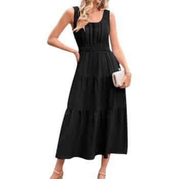 A woman wearing a sleeveless, long black dress with a gathered waist and tiered skirt, holding a small white clutch. She has wavy blonde hair and is wearing strappy heels.