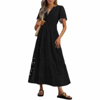 Woman wearing a black, short-sleeve, ankle-length eyelet dress with a v-neck, carrying a beige bag on her shoulder and wearing black sandals.
