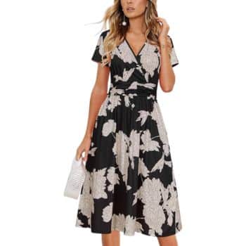 Woman wearing a short-sleeved, black midi dress with a white floral print, holding a white clutch bag.