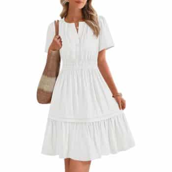 A woman wearing a short-sleeved, white knee-length dress with a gathered waist, holding a woven straw handbag, and accessorized with bracelets.