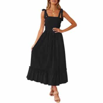 Woman wearing a sleeveless black midi dress with shoulder tie straps and a ruffled hem, paired with strappy sandals, posing with one hand on her hip and the other holding the dress.