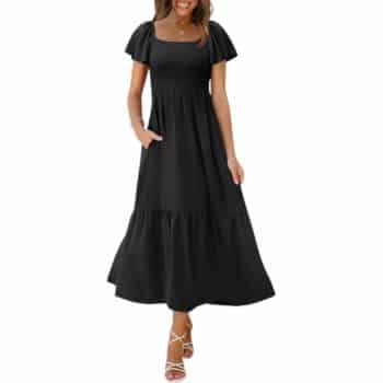 Woman wearing a black, short-sleeve, ankle-length dress with a square neckline, gathered waist, and flared skirt; she is smiling and standing in strappy white sandals.