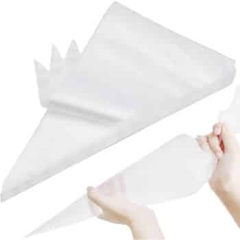 A stack of clear, disposable piping bags, with one bag being held and used by a person’s hands, perfect for icing or decorating my favorite cakes and pastries.