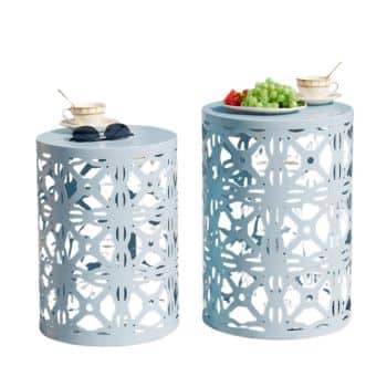 Two cylindrical outdoor tables with intricate cut-out patterns. The left table holds sunglasses and a teacup, while the right displays a teacup alongside a plate of green grapes and strawberries—perfect complements to outdoor tables and chairs.