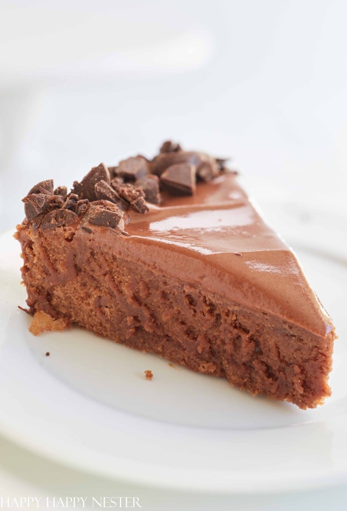 A slice of rich chocolate mousse cake, one of my favorite cakes, sits on a white plate topped with chocolate pieces, its smooth and creamy texture visible on the cake's surface.