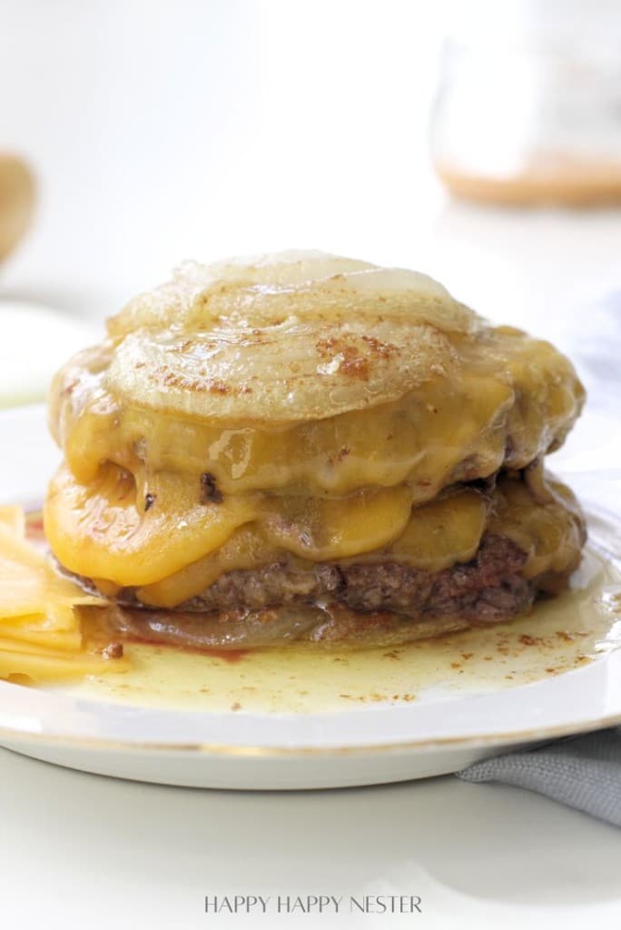 A stack of cheesy, melted French onion soup burgers inspired by the In-N-Out Burger Recipe (Flying Dutchman), topped with caramelized onions and gooey cheese, with savory juices and melty cheese pooling at the bottom.